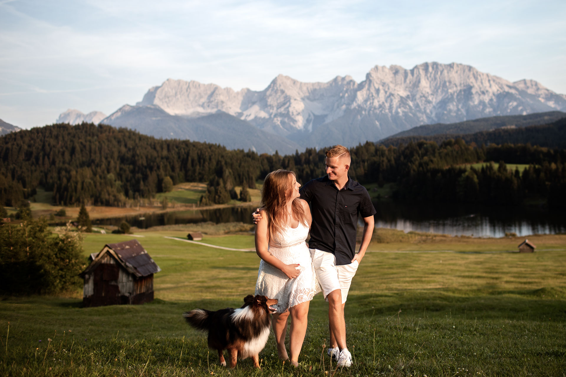 Dieses natürliches Hundefoto ist in Walgau vor den Alpen in Bayern entstanden. Zusehen ist ein Mann und ene Frau, die mit ihrem Hund vor einem Bergpanorama spazieren gehen.